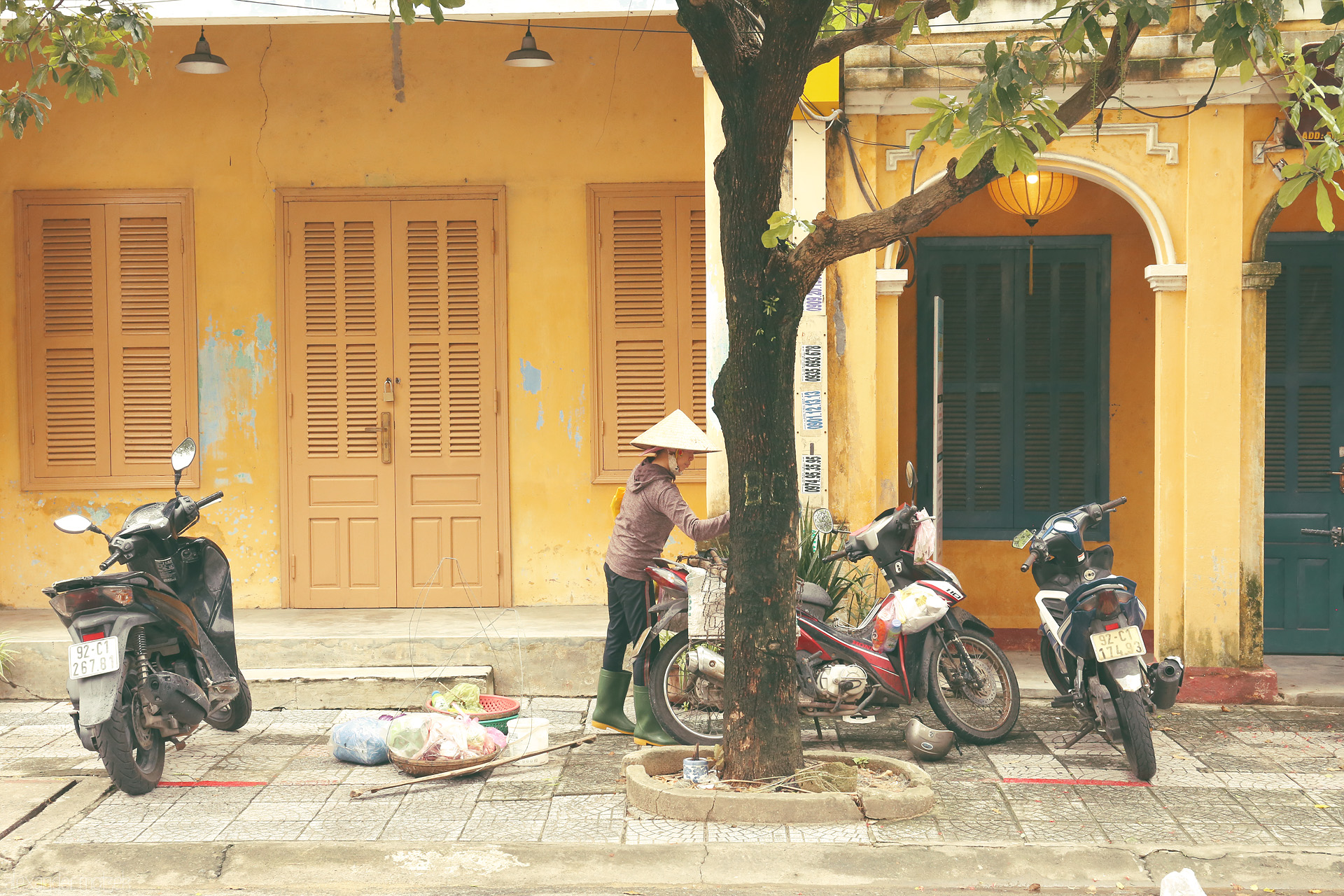 Amber Hues of Hoi An Foto von A woman in a nón lá hat, street vendors’ baskets, and scooters beneath Hoi An’s golden walls and lanterns. Morning unfolds, Vietnam style.