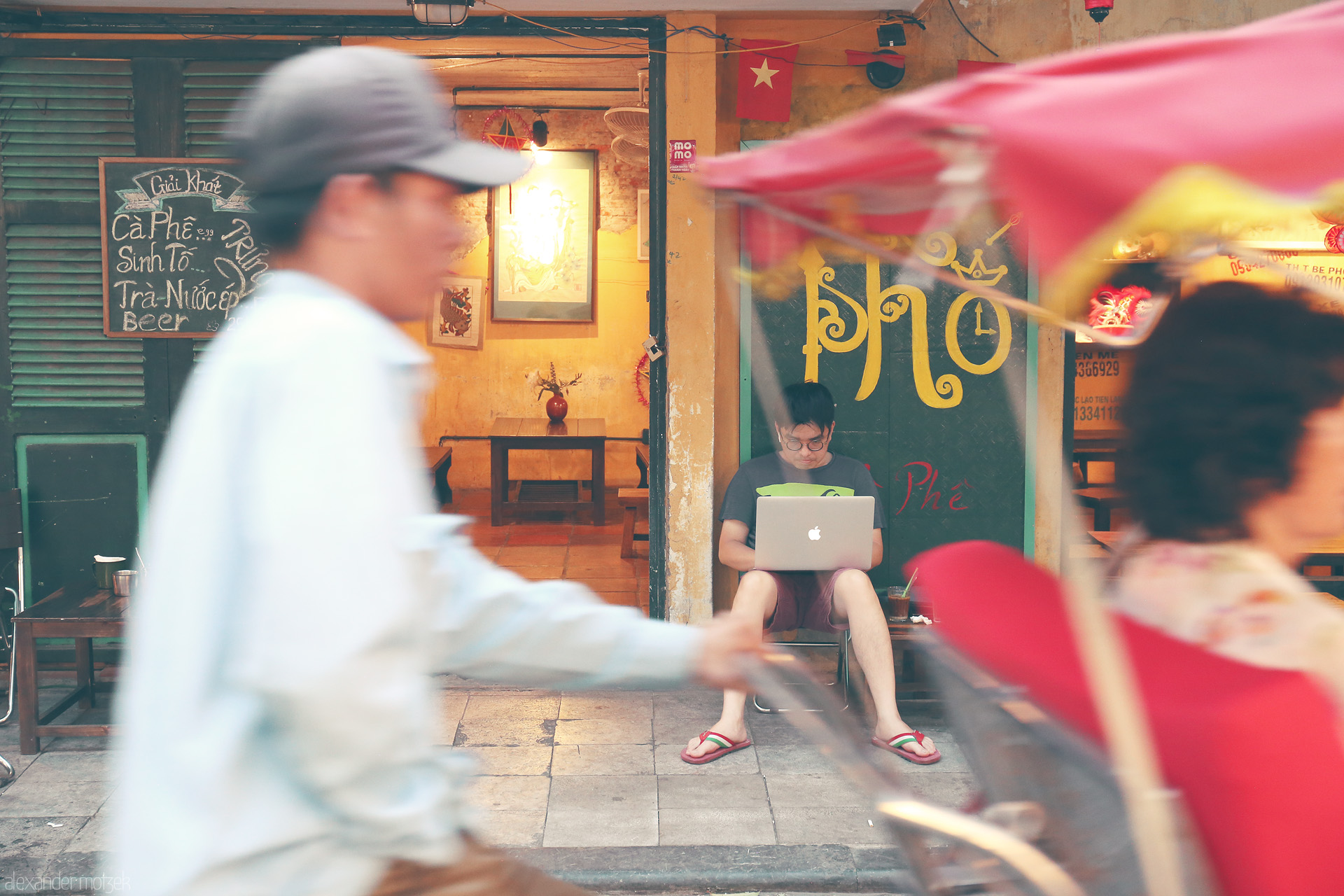 Pho & Pixels Foto von A young man works on a laptop amid street bustle outside a cozy cafe in Phuong Hàng Bac, Hanoi—modern life in a timeless scene.