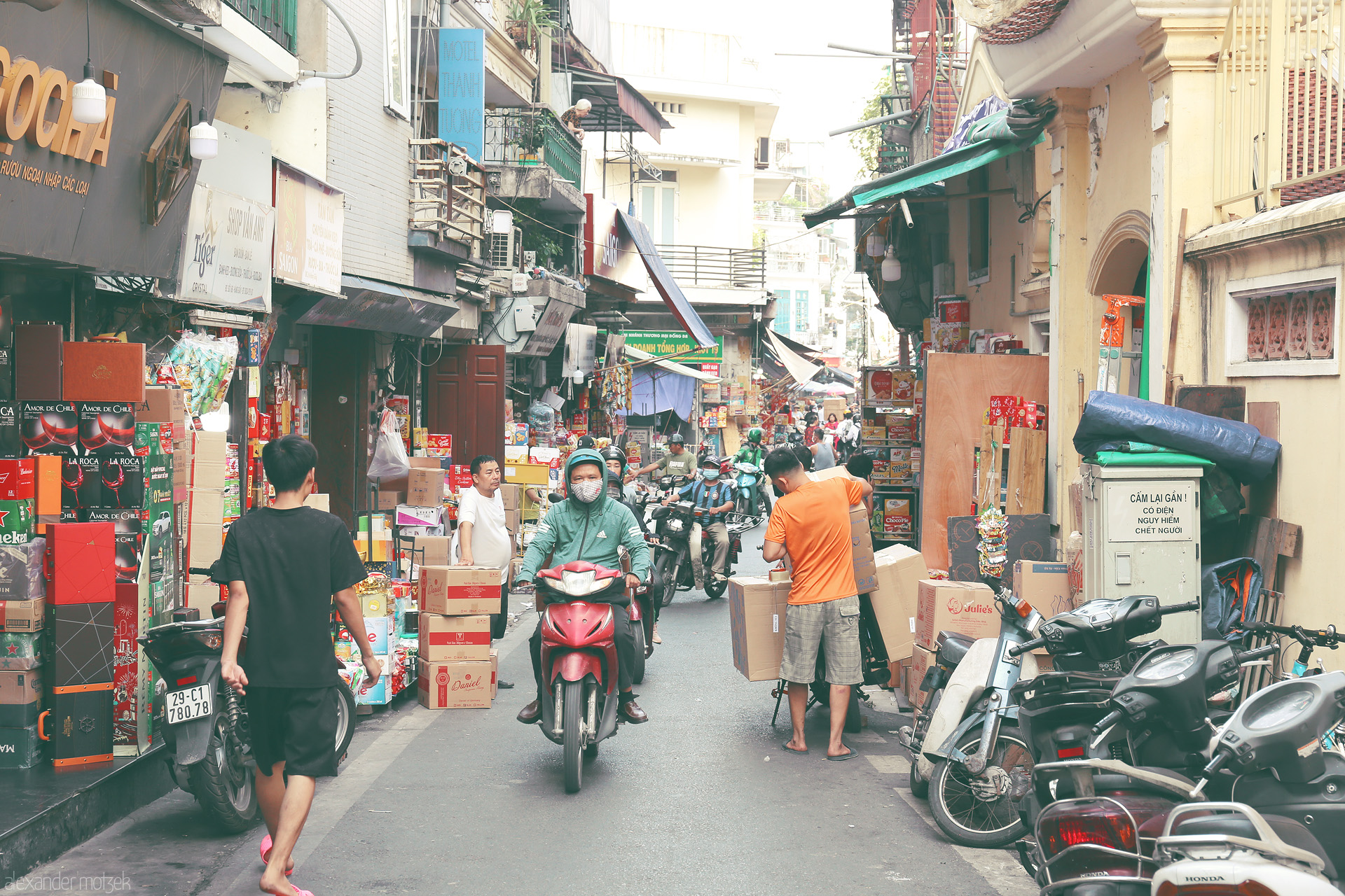 Old Quarter Overture Foto von Bustling alley of Hàng Buồm, Hanoi, alive with scooters, stacked boxes, and vibrant daily street life.
