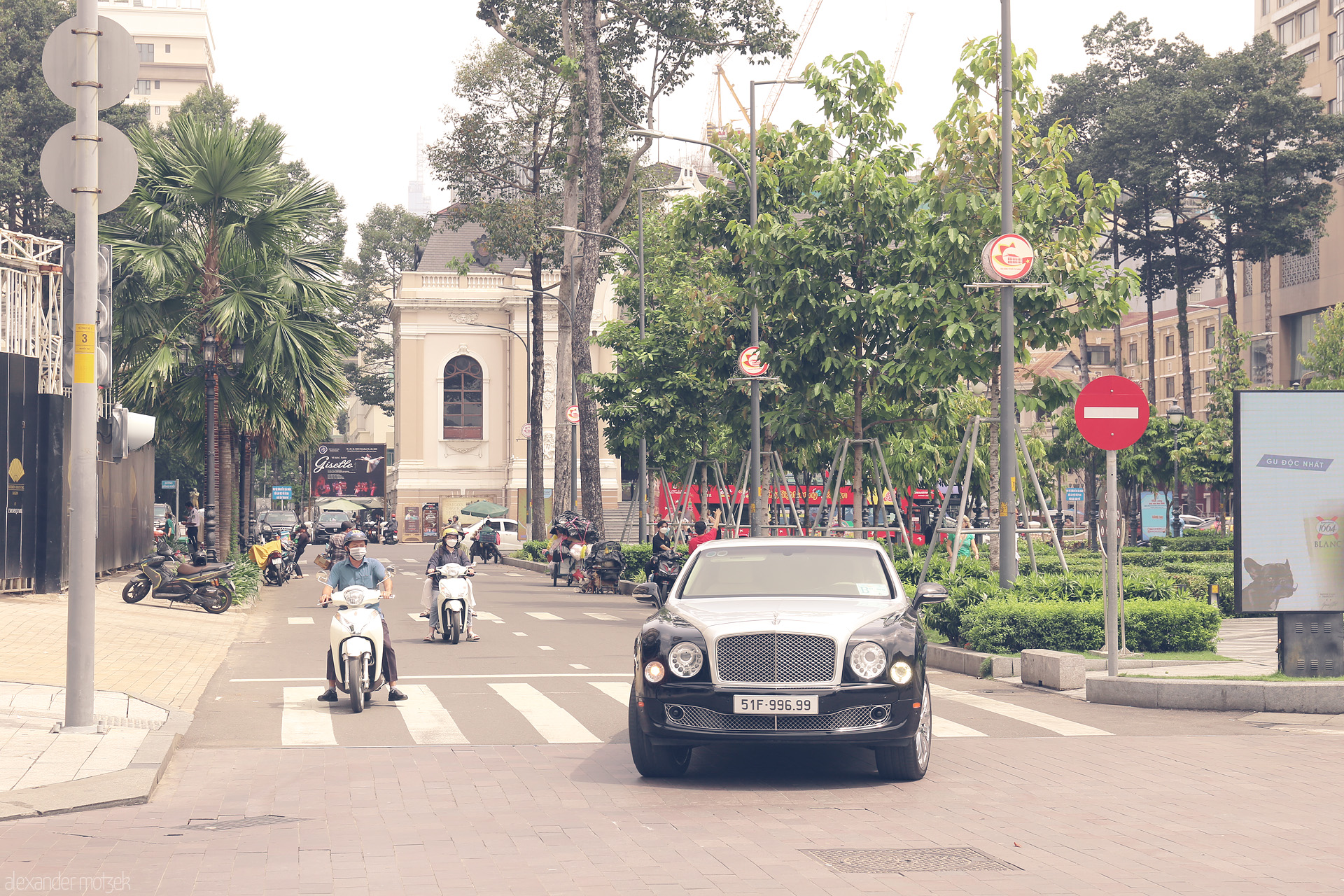 Bentley & Bánh Mì Streets Foto von Contrasts of Ho Chi Minh City: a Bentley glides past scooters and colonial echoes in lush, sunlit Saigon.