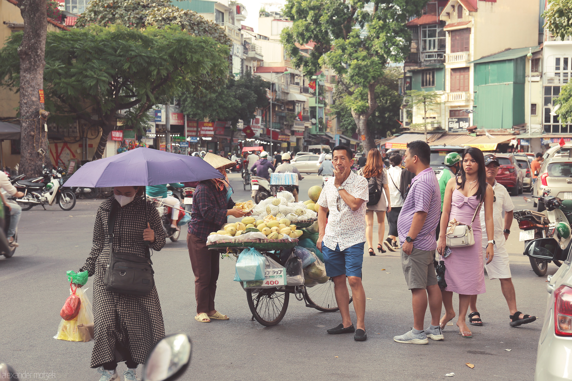 Umbrella & Dua Foto von Daily life unfolds on Dong Xuan’s bustling corner, street vendors, fruits, and city dwellers glowing under Hanoi’s urban tapestry.