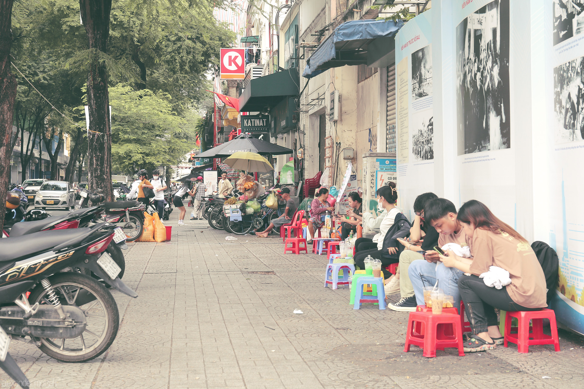 Saigon Sáng: Sidewalk Stories Foto von Locals gather on tiny stools, sipping iced coffee beneath urban trees in vibrant Saigon, Vietnam—where street life tells a thousand tales.