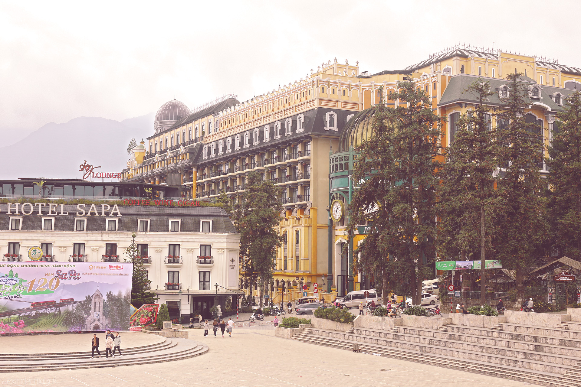 Heritage in the Hills Foto von Majestic hotels rise through misty Sapa, Vietnam—French Indochine meets mountain serenity in a lively plaza framed by pines.