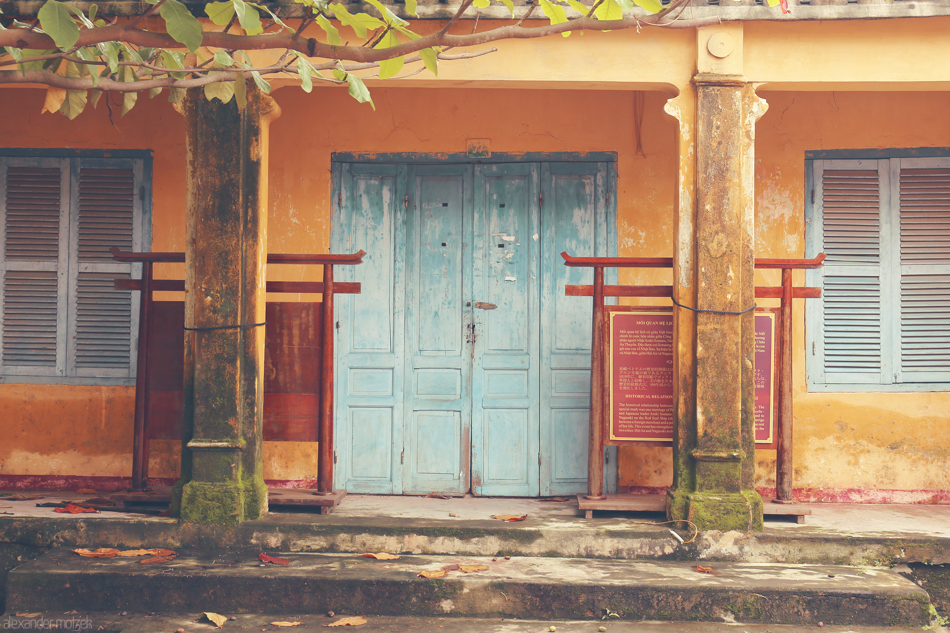 Hoi An Hues Foto von Moss-draped columns and faded blue doors in Hoi An, Vietnam evoke tranquil tales of history and time.