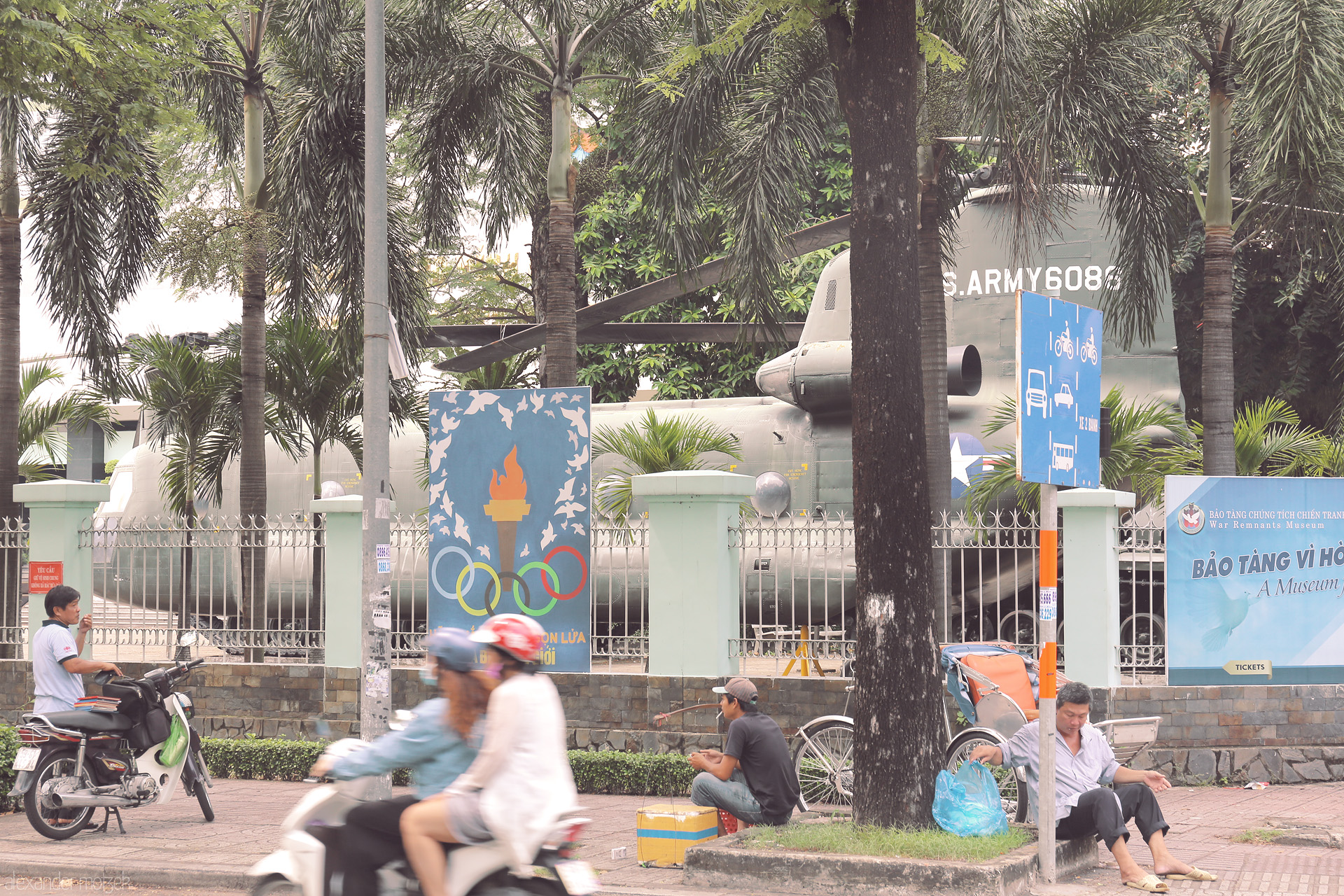 Palms, Rotors, and Streetlife Foto von Motorbikes speed past the War Remnants Museum in Saigon, where echoes of conflict meet the daily pulse of Vietnamese city life.