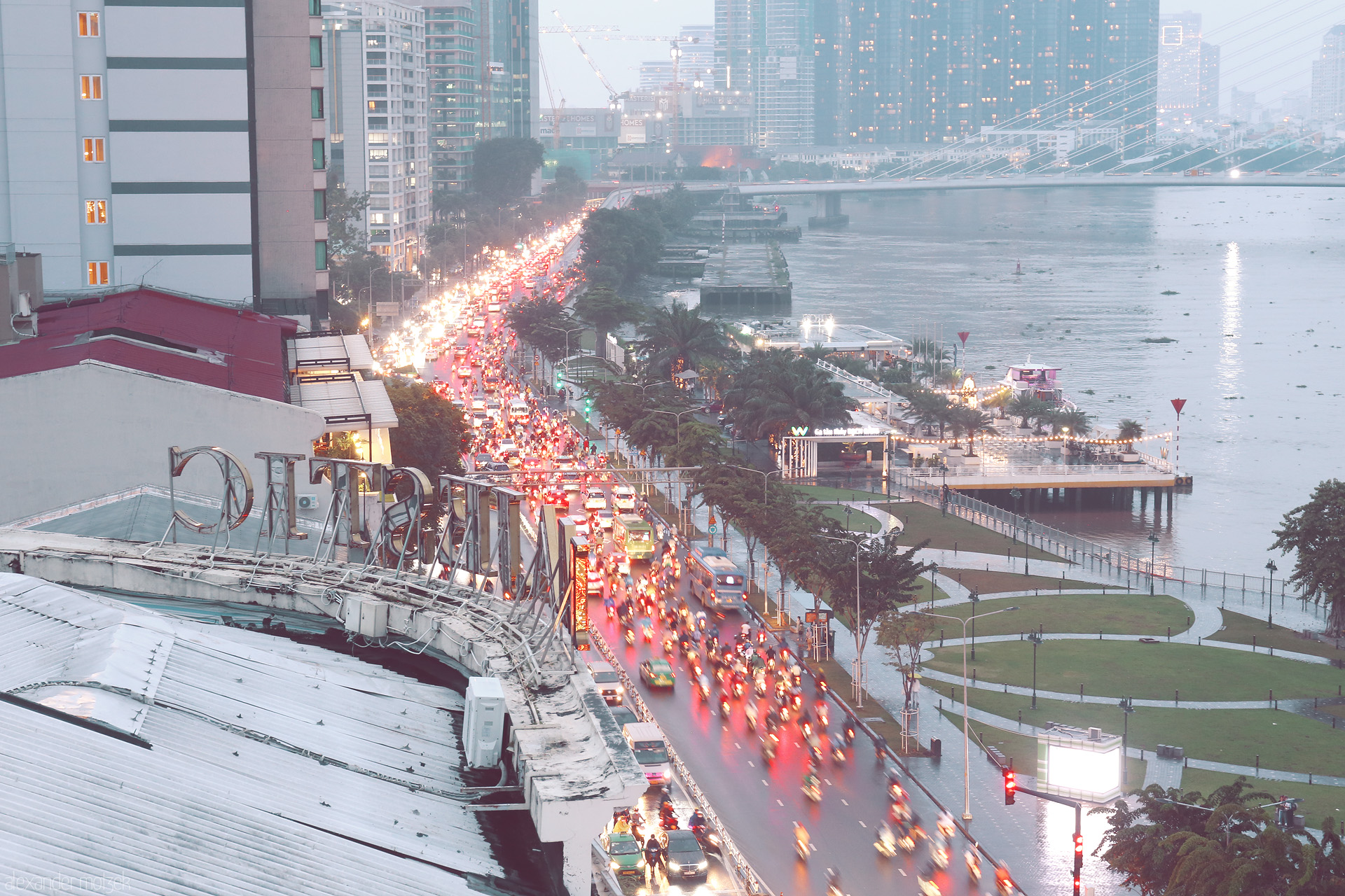 Sông Sài Gòn Hustle Foto von Rush hour veils Saigon’s Bach Dang riverside in lights, where dỏ xe máy flow beside the tranquil Sông Sài Gòn, city pulse meets water calm.