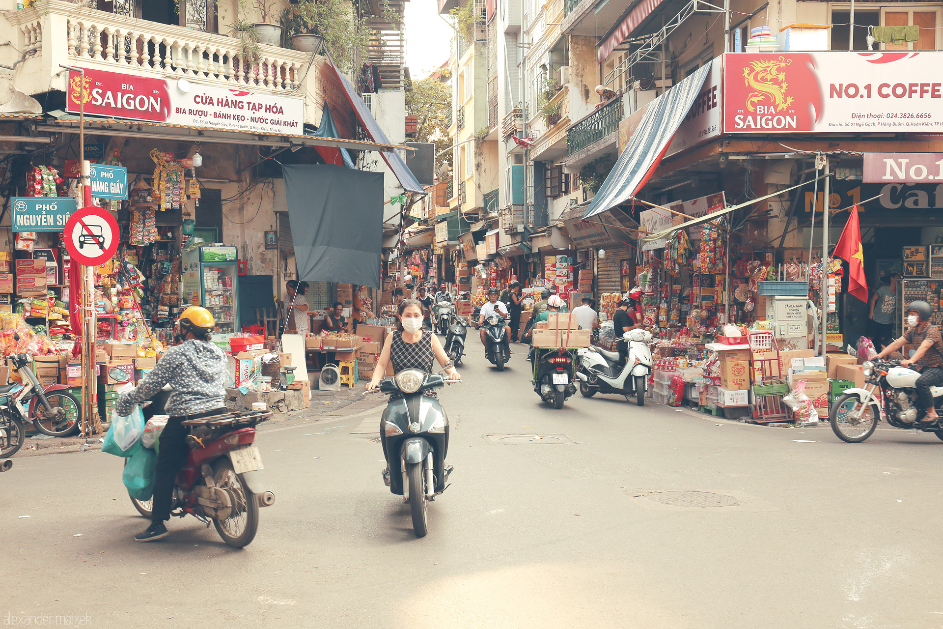 Hanoi’s Urban Pulse Foto von Scooters weave between vibrant street stalls in Phuong Hàng Buom, Hanoi, alive with color, commerce, and the energy of daily city life.