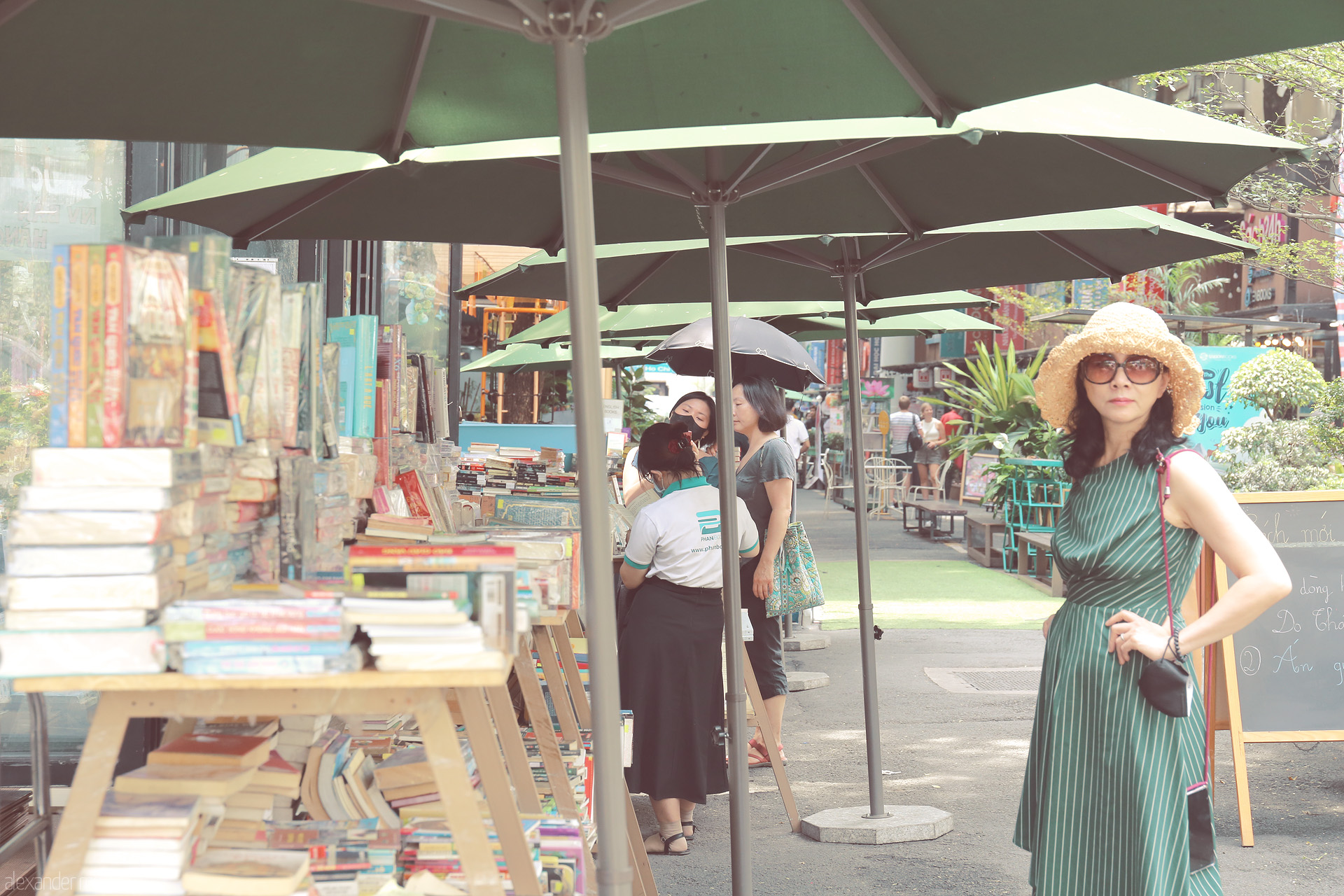 Sách & Shade: Saigon Foto von Under green umbrellas on Saigon’s Book Street, a woman in sunglasses captures the spirit of literary HCMC. Vietnam vibrance, sun, and stories.