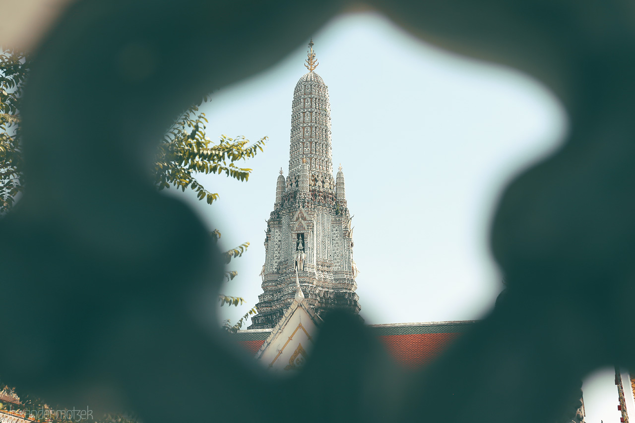 Chao Phraya Serenity Foto von Wat Arun's spire, framed through ornate lattice, stands tall by the Chao Phraya River, Bangkok, capturing serene elegance and architectural beauty.